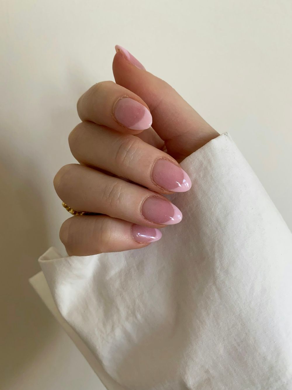 Mano con uñas almendra rosadas sobre una tela blanca
